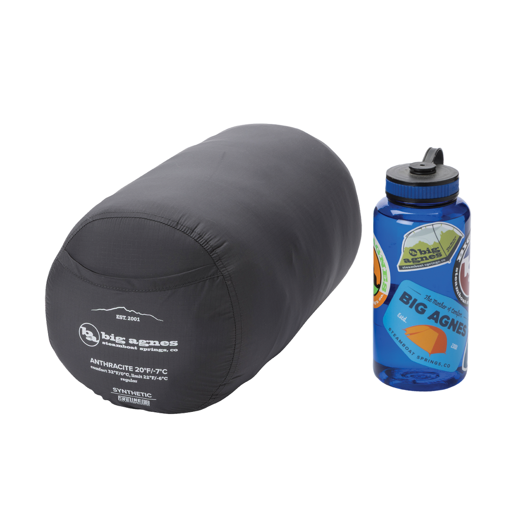 A Big Agnes Returns Anthracite 20° gray mummy sleeping bag in its compression sack sits beside a blue sticker-covered reusable water bottle, both on a white background.