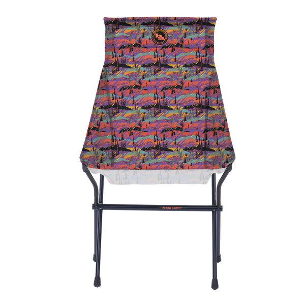 The Big Agnes Returns Big Six Camp Chair - Alpenglow is a lightweight, packable camp chair with a black metal frame and a colorful seat featuring a vibrant abstract mountain landscape in red, purple, blue, and orange.