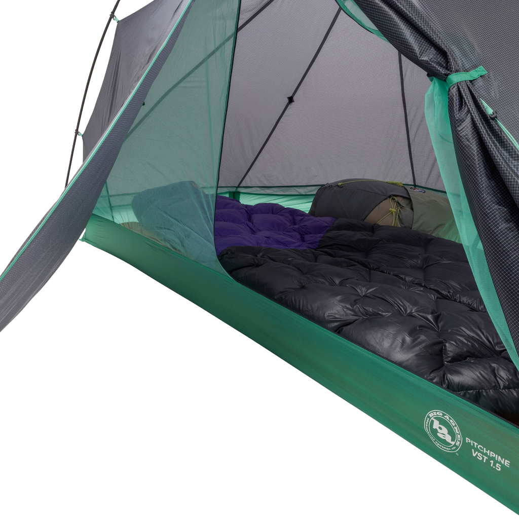 A close-up of the Big Agnes Returns Pitchpine VST 1.5 tent interior reveals two sleeping bags side by side on the floor, with mesh sides and a partially open door in this ultralight green and grey shelter.