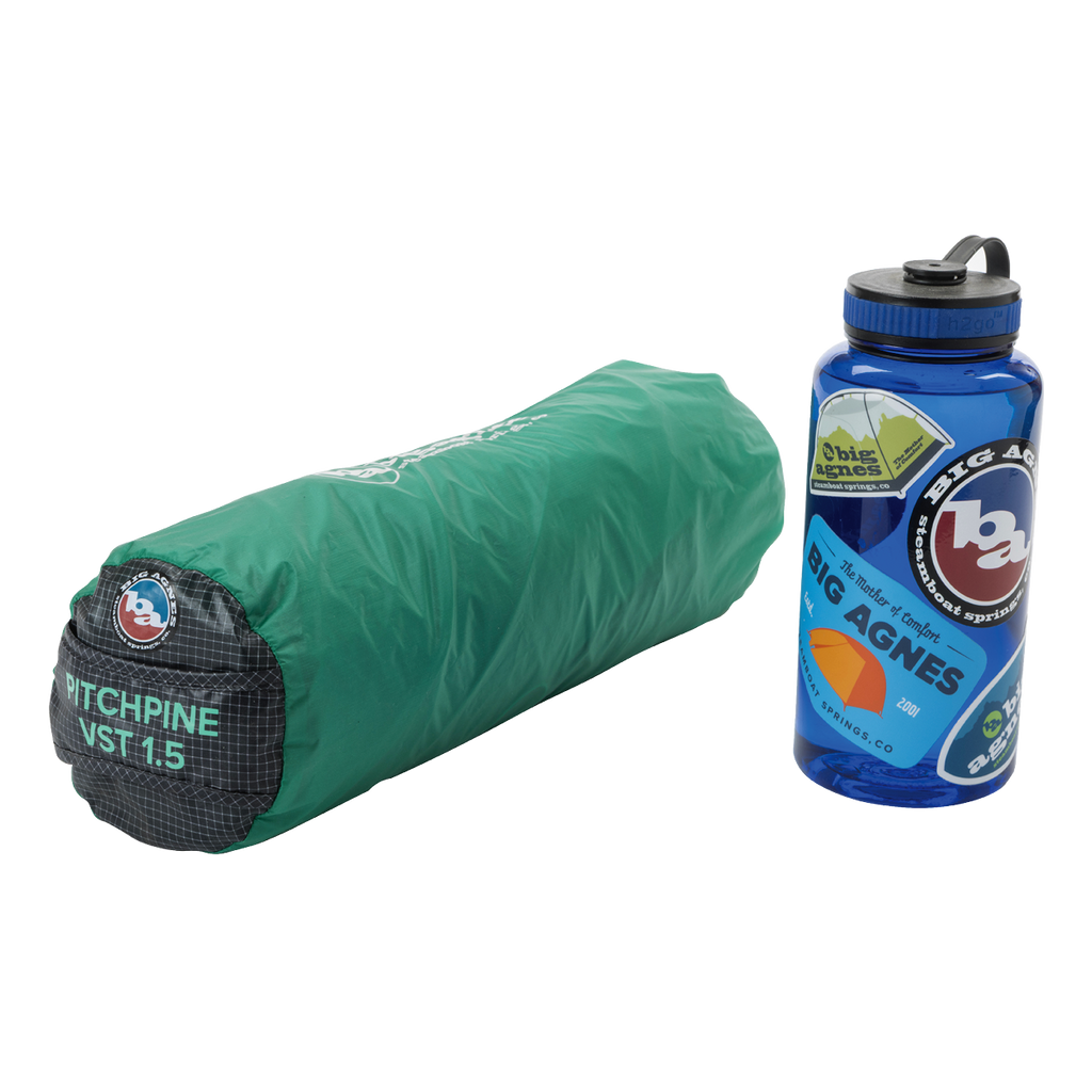 A rolled-up green Big Agnes Returns Pitchpine VST 1.5 ultralight shelter sits next to a blue water bottle decorated with Big Agnes Returns stickers.