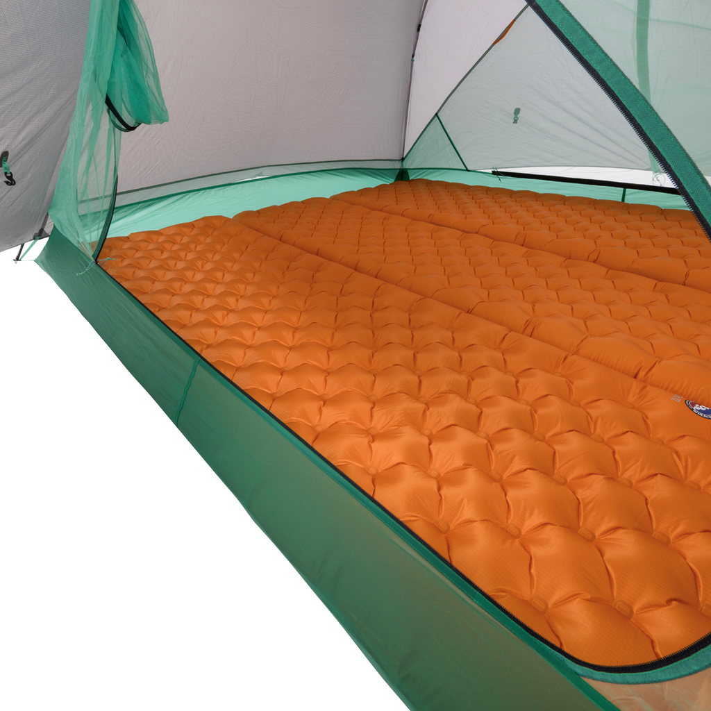 Orange inflatable sleeping pads are arranged side by side inside a green Big Agnes Returns Sarvis VST 2 tent, covering the floor and offering cushioning for campers in this ultralight shelter.
