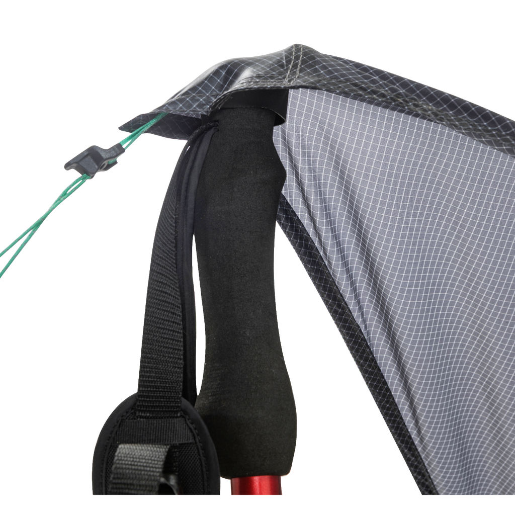 Close-up of the Big Agnes Returns String Ridge VST 1.5, with a trekking pole supporting the tent’s black and gray fabric corner, black strap, and green guyline with a plastic tensioner in this ultralight shelter setup.
