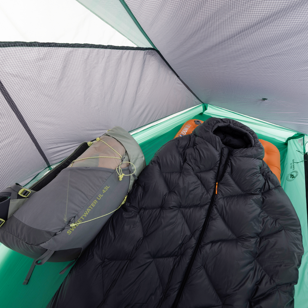 A sleeping bag and gray backpack are inside a light green Big Agnes Returns String Ridge VST 1.5 tent. Its mesh roof and sides are visible, with a sleeping pad beneath the bag—making this ultralight tent perfect for outdoor adventures.