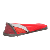 A red and gray Big Agnes Three Wire Hooped Bivy sits with its side partly open, displaying an orange sleeping bag inside. The low-profile, one-person bivy offers four-season protection and is shown against a plain white background.