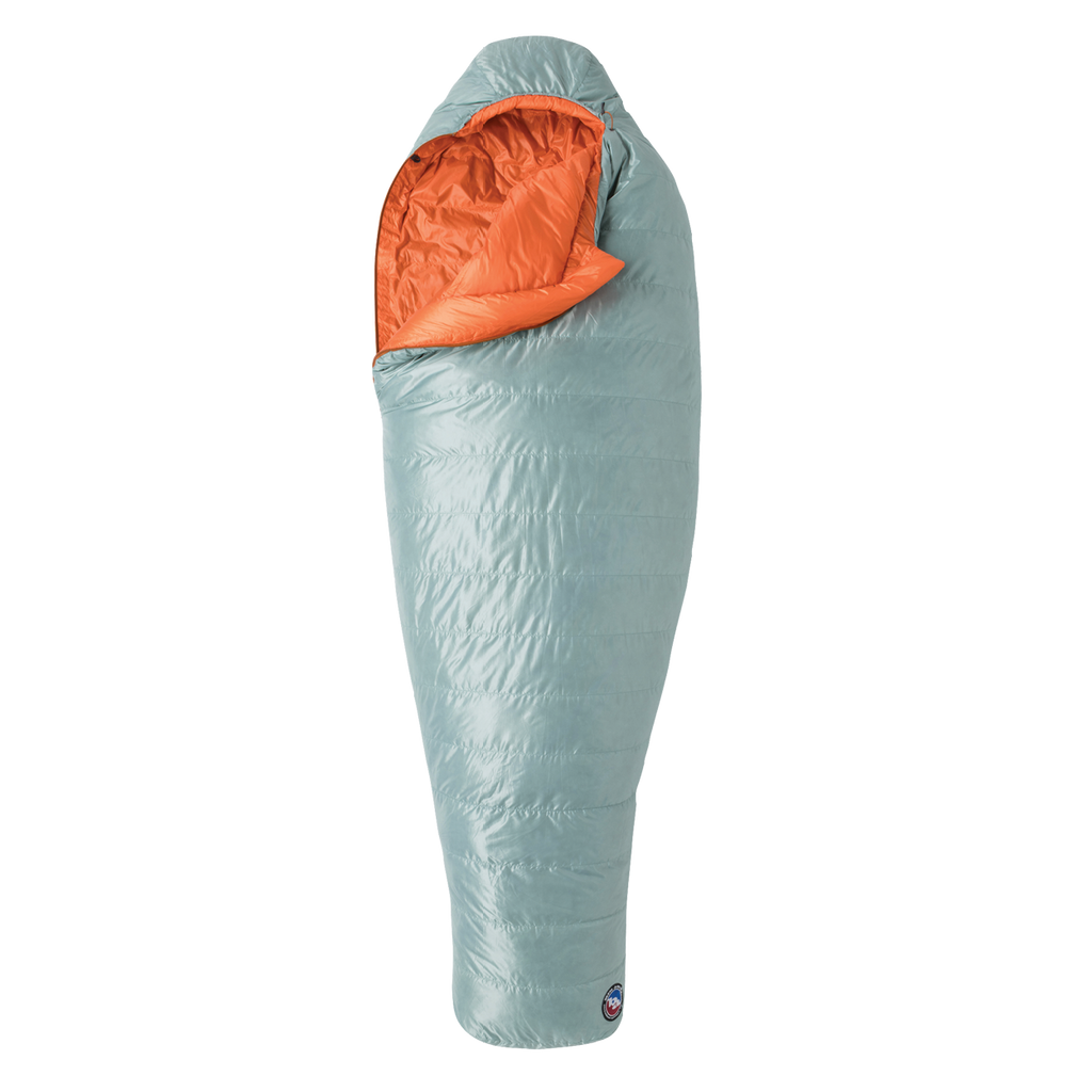 The Big Agnes Returns Women's Greystone 30° sleeping bag in light blue, featuring DownTek insulation, stands upright against a white background. Its mummy-style hood is slightly open, showing the bright orange interior lining.